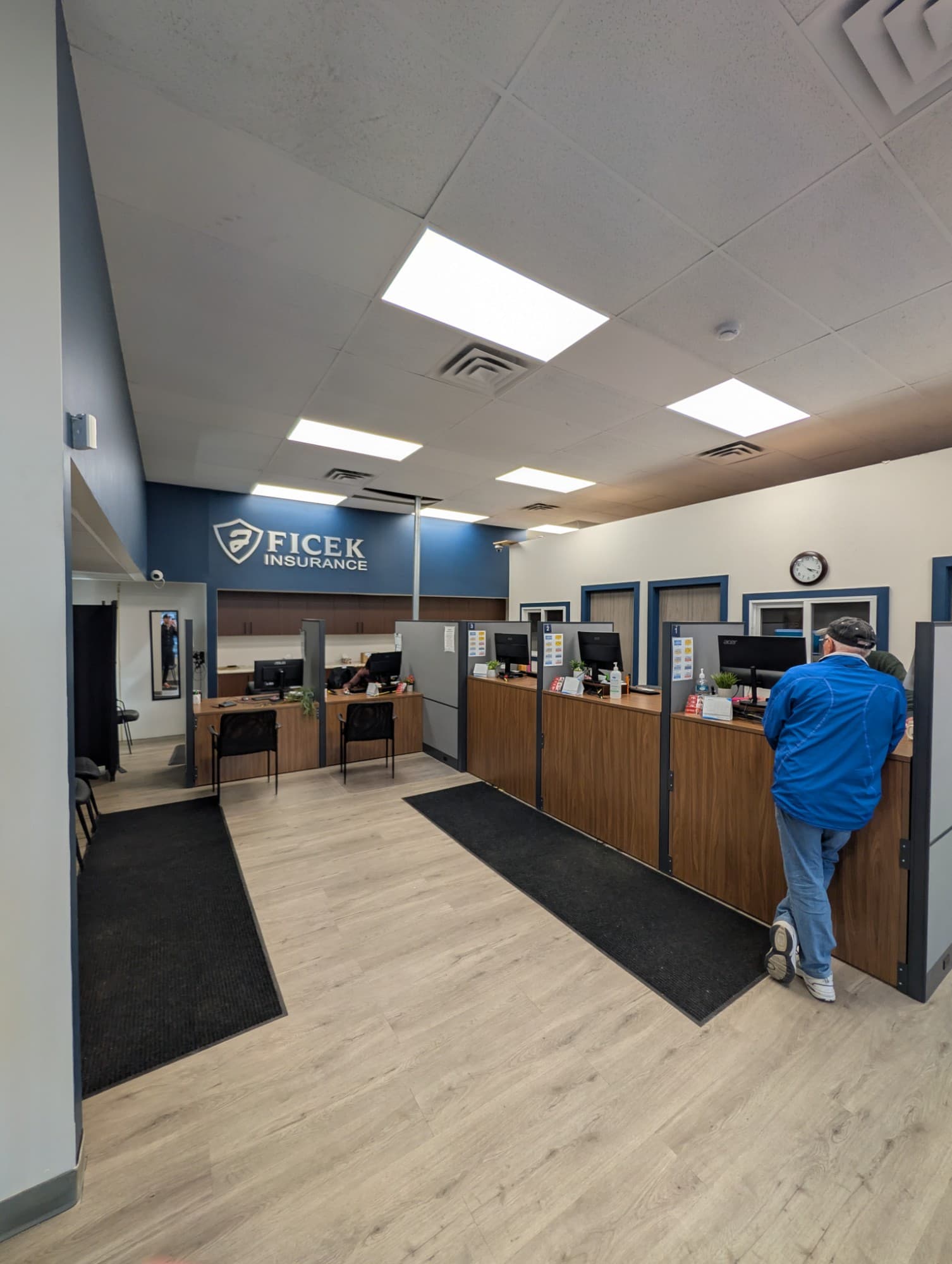 Inside the 18th Street office: a row of numbered service wickets along a wood counter, under the Ficek Insurance sign on the blue feature wall.